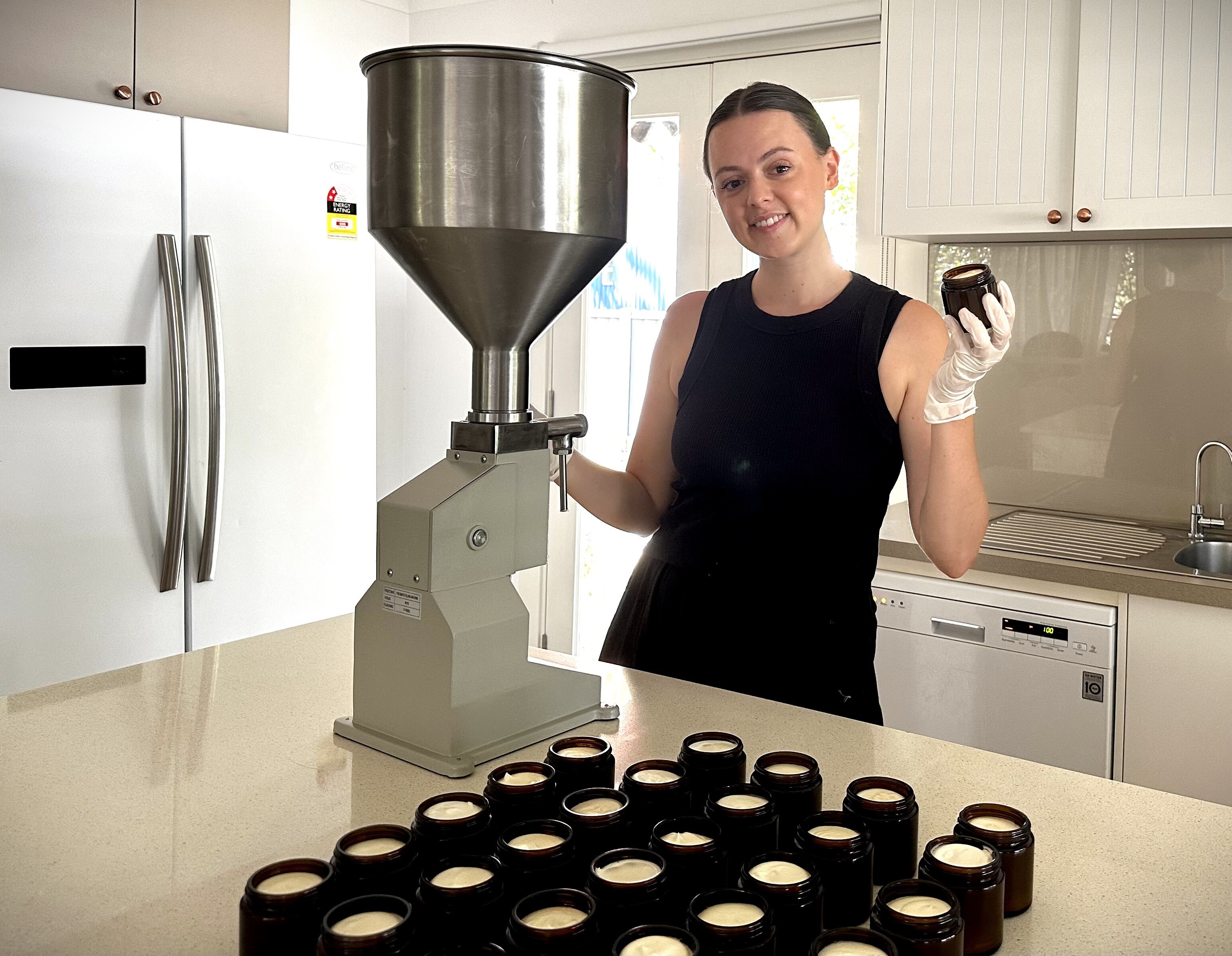 A young woman stands next to a batch of jars filled with tallow products.