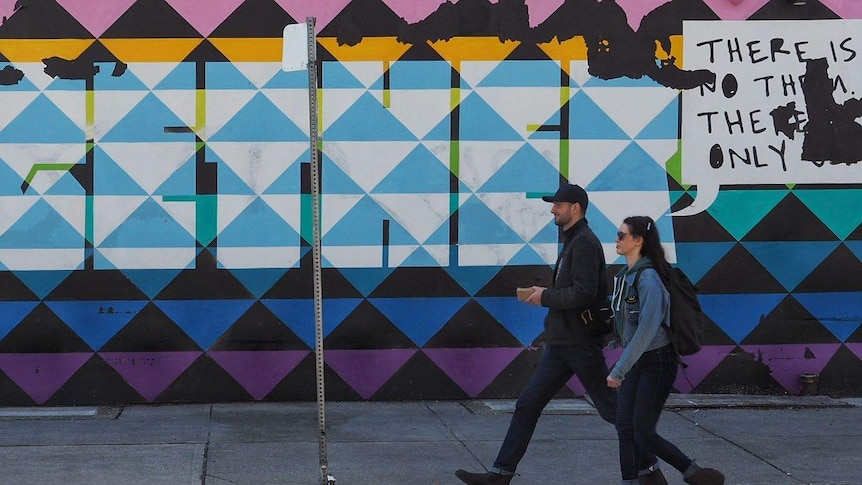 Two people in denim stride past a colourful mural