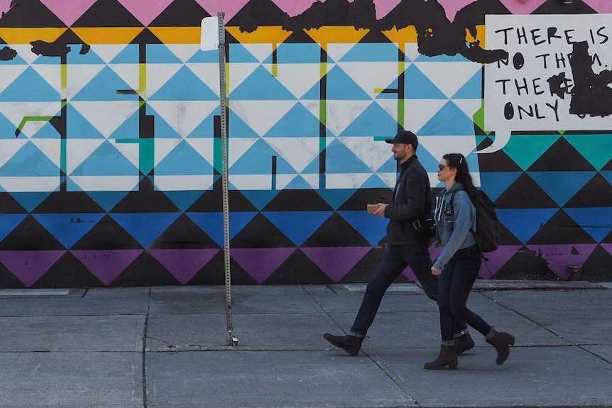 Two people in denim stride past a colourful mural