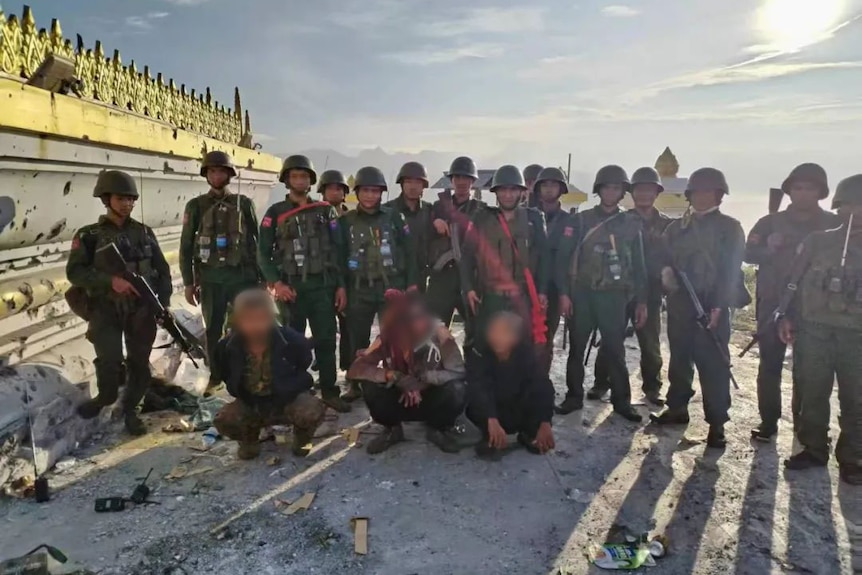 A group of MNDAA soldiers pose for a photo with three captured enemies.