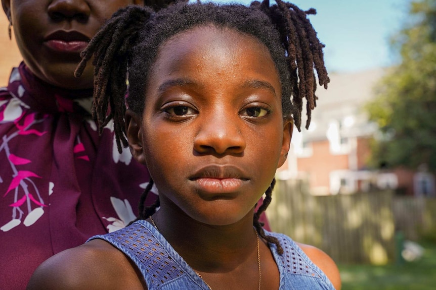 A little girl with her mother behind her looking serious