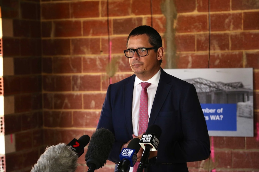 Treasurer Ben Wyatt stands before microphones at a media conference in a building site in Perth, WA.