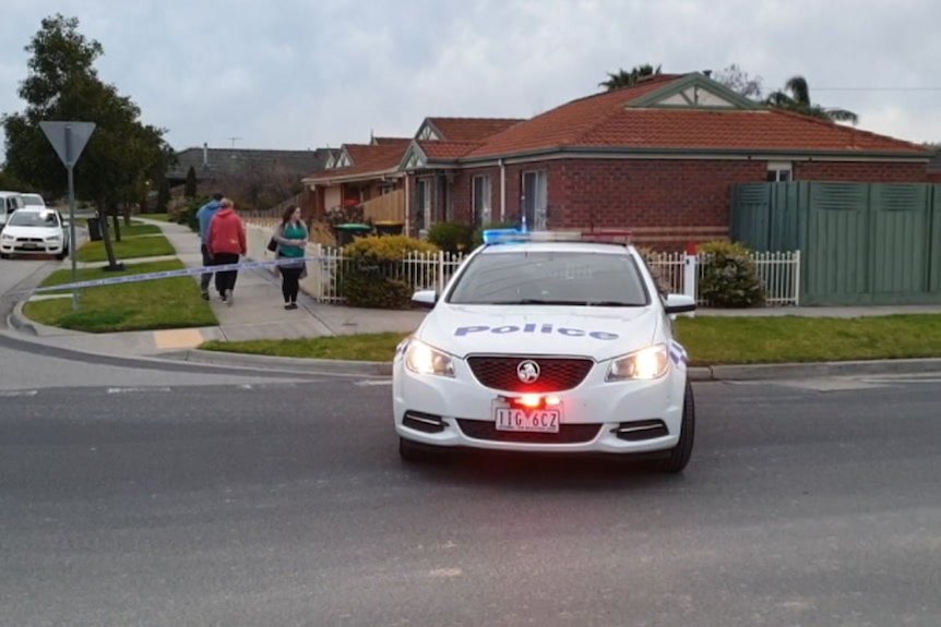 A police car sits on a road in front of a brick house.