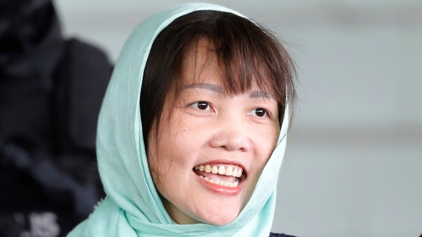 A woman wearing a headscarf smiles as she is lead from court.