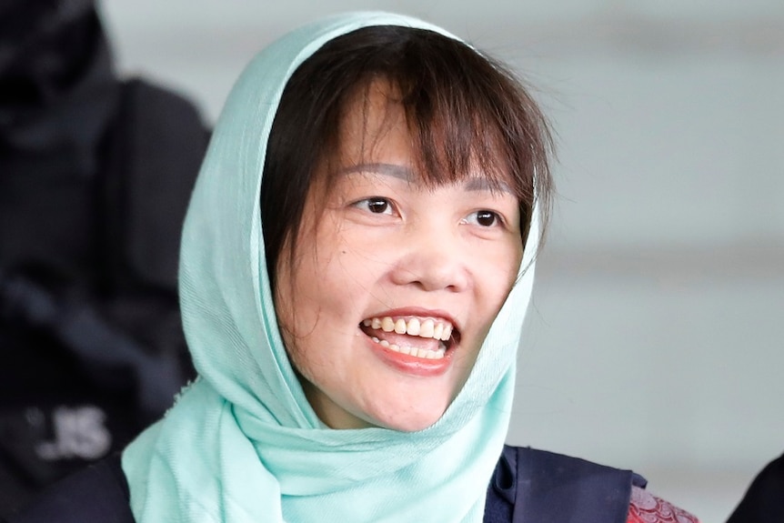 A woman wearing a headscarf smiles as she is lead from court.
