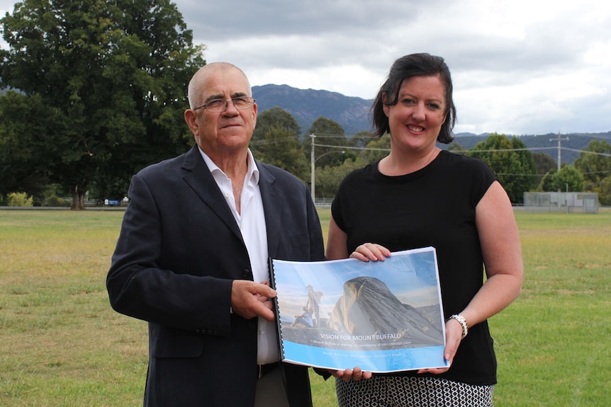 David Jacobson and Janelle Boynton stand an oval with Mount Buffalo in the background holding a document together