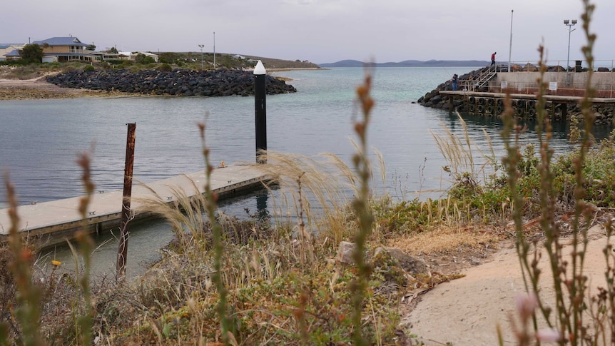A marina with a jetty and a couple of fisherman is in the foreground, with Spencer Gulf in the background.