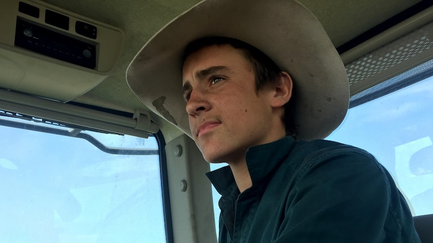 A close-up shot of Jack Johnstone, wearing a hat and sitting in a harvester.