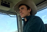 A close-up shot of Jack Johnstone, wearing a hat and sitting in a harvester.