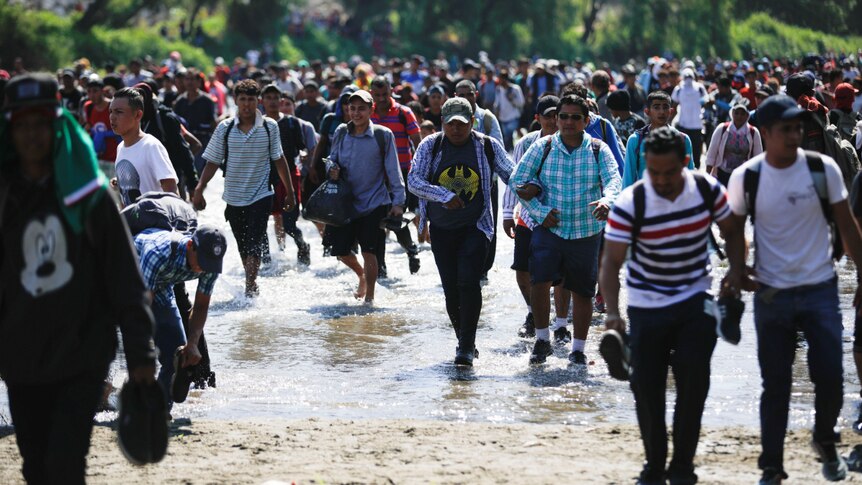 a large group of migrants walk across the Suchiate river into Mexico