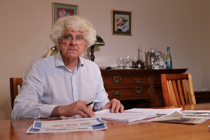 Hugh Selby sits with his legal documents in his dining room.