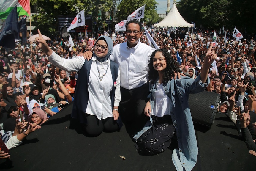 A middle-aged man wearing a white shirt and glasses stood flanked by a veiled woman and a curly girl.