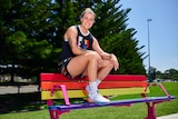 An athlete wearing rainbow clothes sits on a park bench painted with different colours on a sunny day