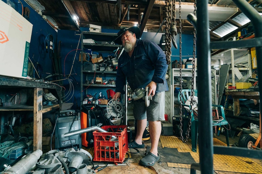 Anthony Gerrets picking up a hub cap and other bits of plastics in a very cluttered workshop.