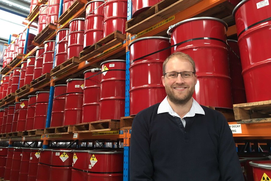James Hardiman stands in front of shelves of barrels at ANSTO.