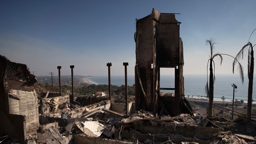 The burned and exposed insides of a destroyed home sit in the foreground of a wide shot of the Californian coast.