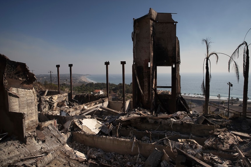 The burned and exposed insides of a destroyed home sit in the foreground of a wide shot of the Californian coast.