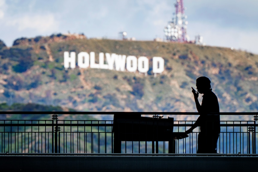 A worker wheels equipment past the famous Hollywood sign.