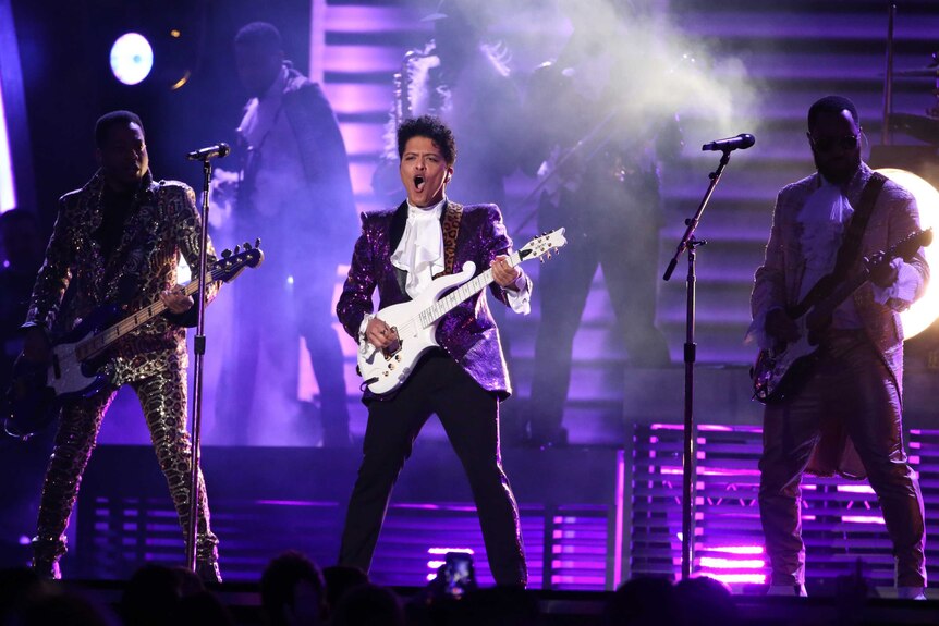 Bruno Mars wears a purple jacket and plays guitar during a Prince tribute at the Grammys