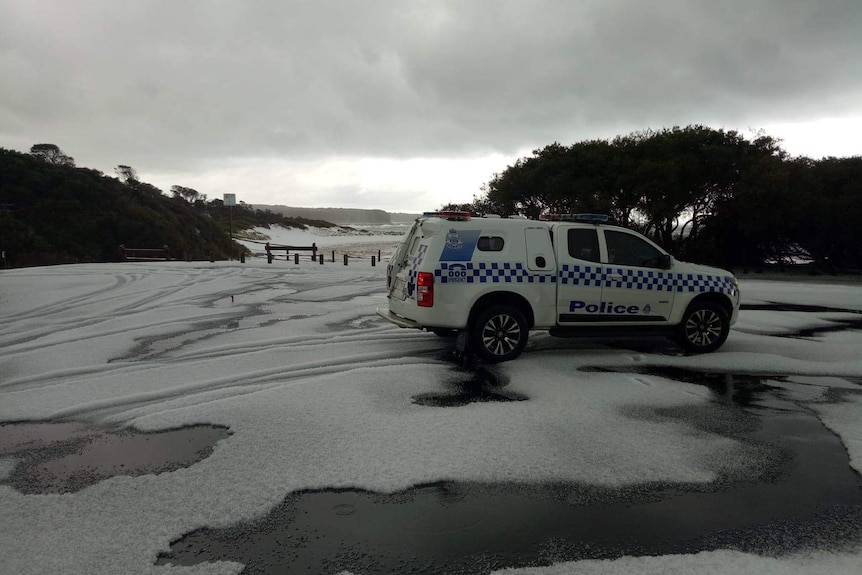 A police car sits on a thick, white blanket of hail under grey skies at a beach.
