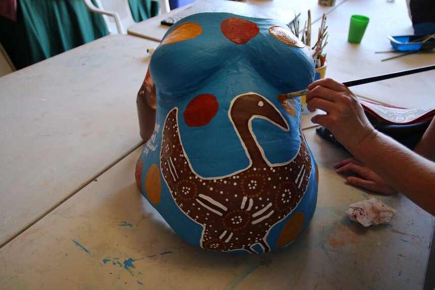 A woman paints a life-size plaster cast of her belly at the Gomeroi gaaynggal centre in Tamworth.