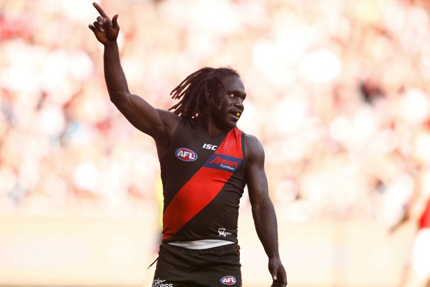 An AFL player raises his right arm to celebrate a goal