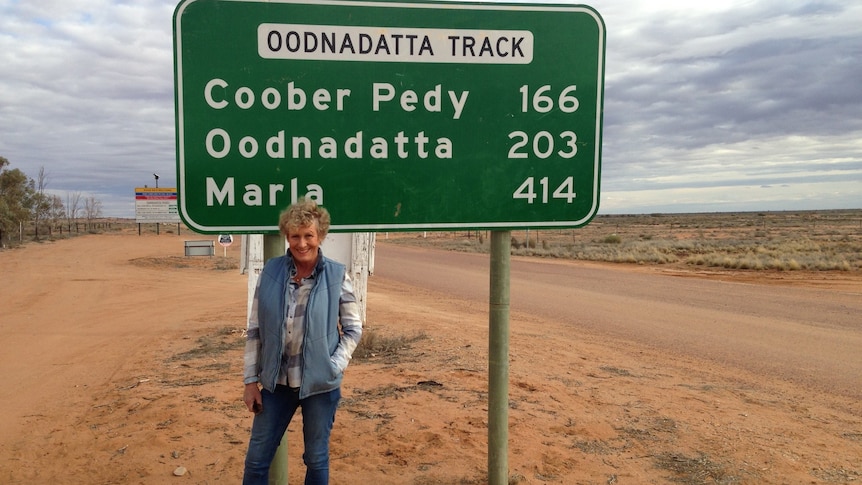 Heather Ewart stands in front of a road sign on the Oodnadatta Track.