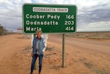 Heather Ewart stands in front of a road sign on the Oodnadatta Track.