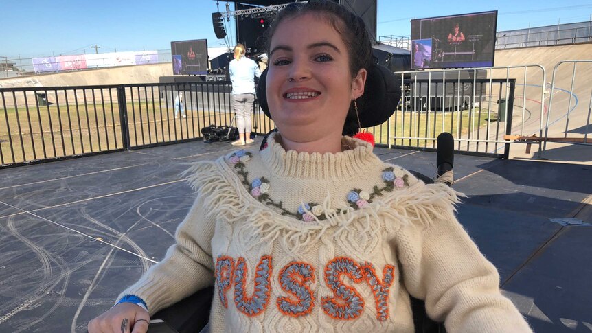 Ashleigh Jamieson wearing a knitted jumper that says "Pussy" and smiling at the camera.