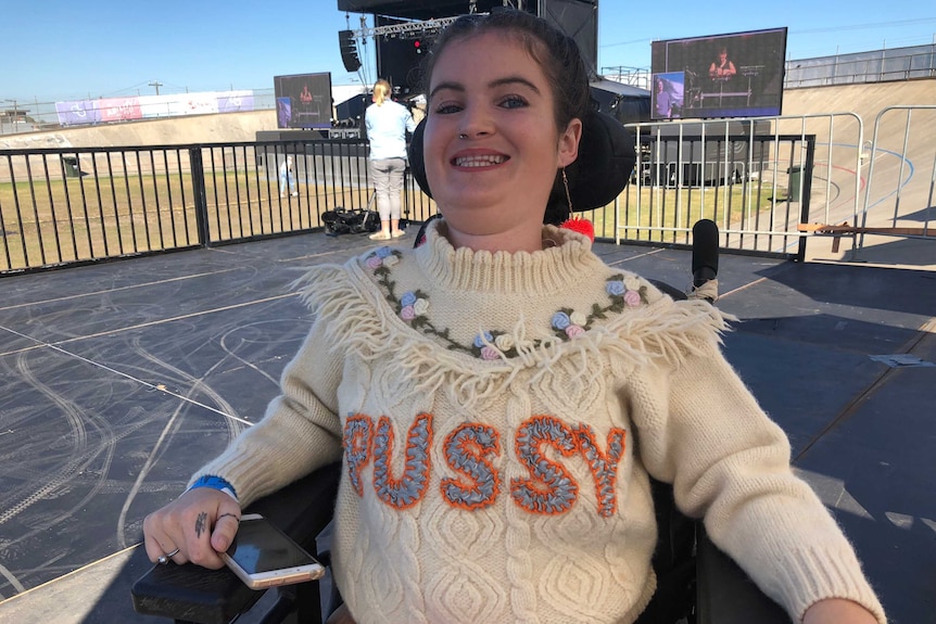 Ashleigh Jamieson wearing a knitted jumper that says "Pussy" and smiling at the camera.