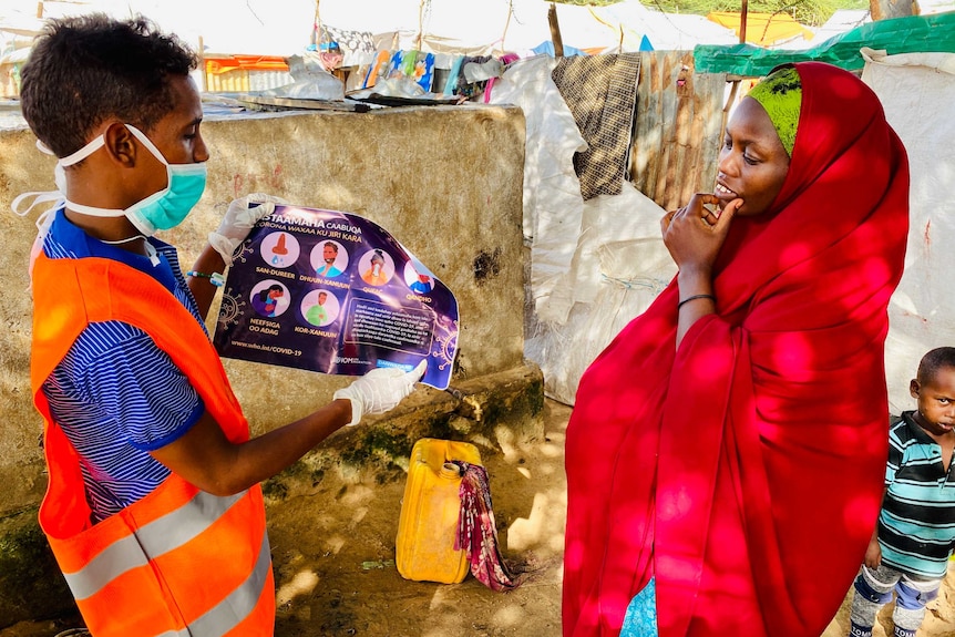 A man wearing a mask shows a woman a pamphlet with health-related instructions.