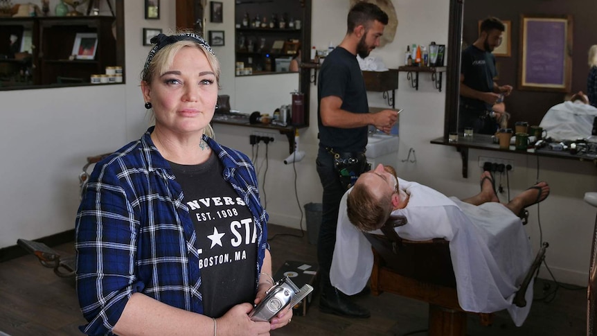 Hairdresser Cassandra Jones stands in her barbering salon Gentleman Jones while a barber shaves a client.