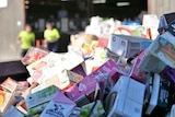 Different sized and coloured cartons including juice and milk poppers, processing shed and workers in background.