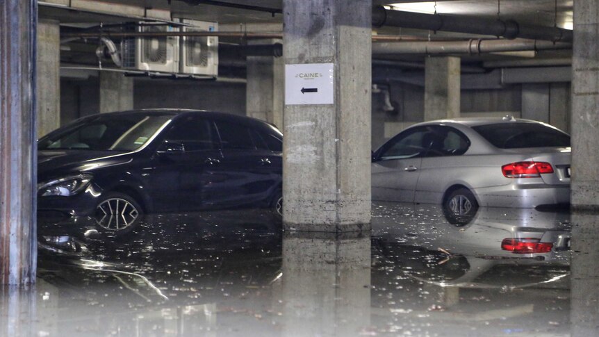 Water rises up the sides of two cars in an underground car park