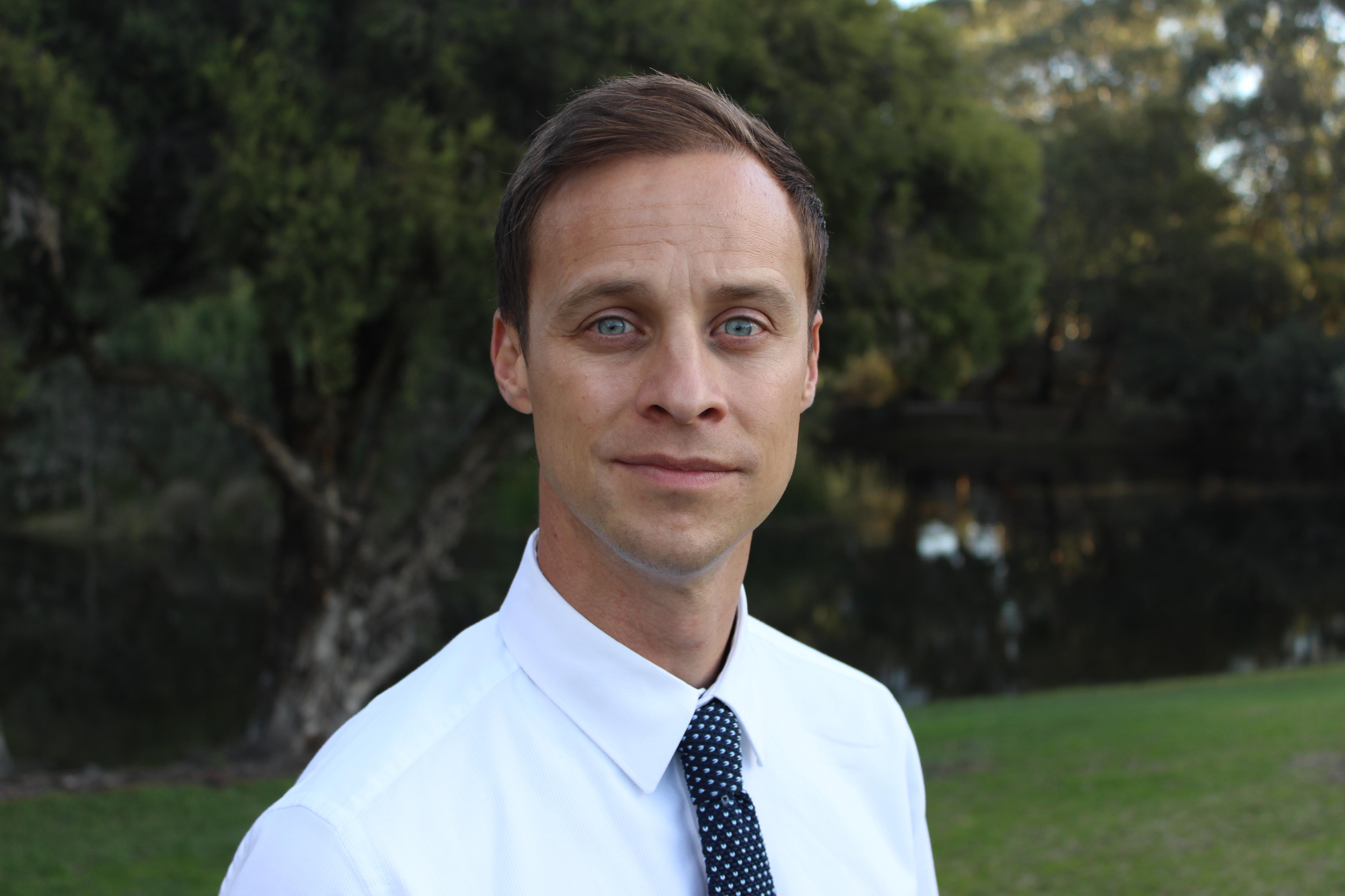 Man in white shirt and dark tie looks at camera