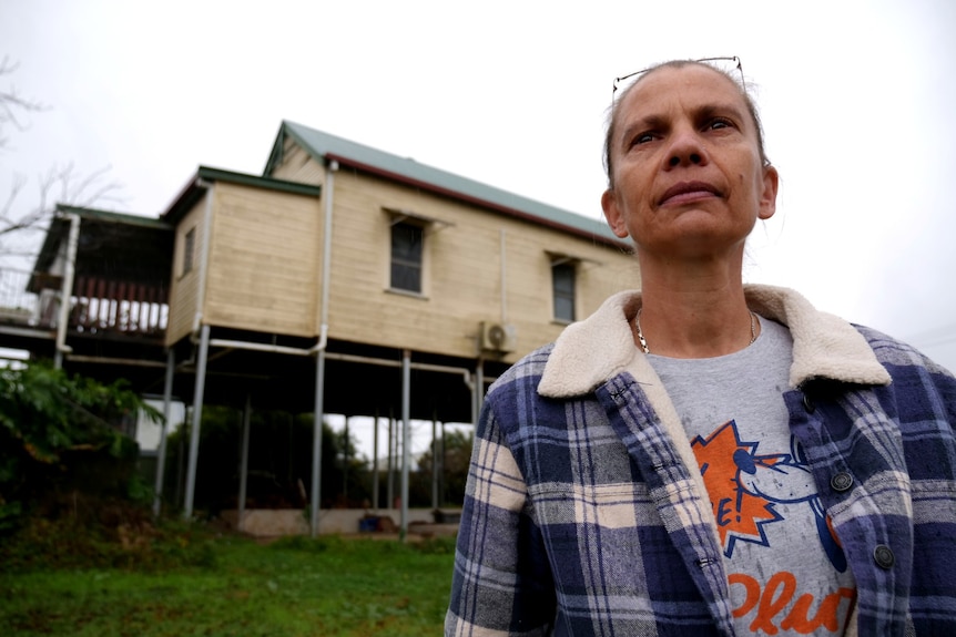 A woman in a flannelette shirt with a house on stilts in the background