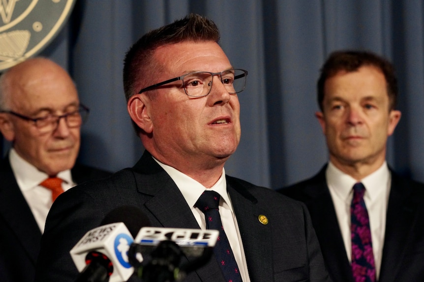 A man in a suit speaking at a press conference.