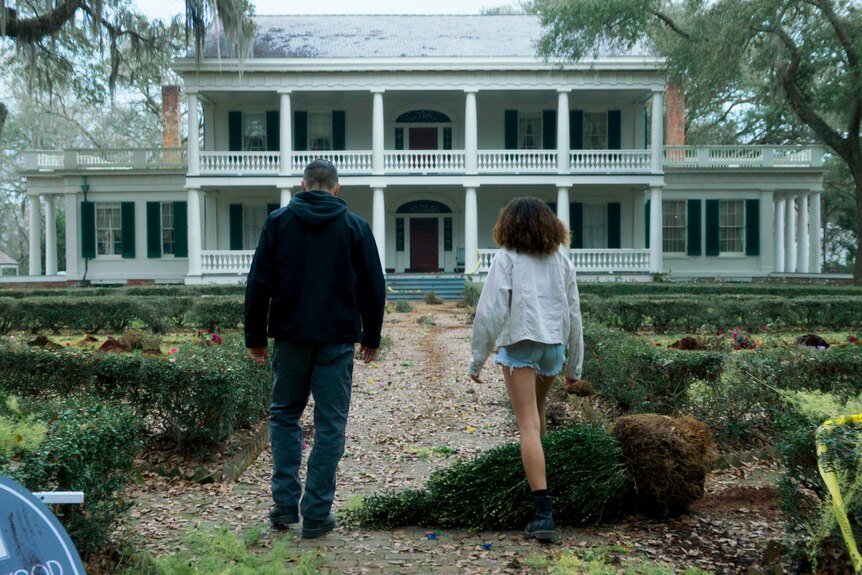 Man and woman walk towards an old white southern mansion.