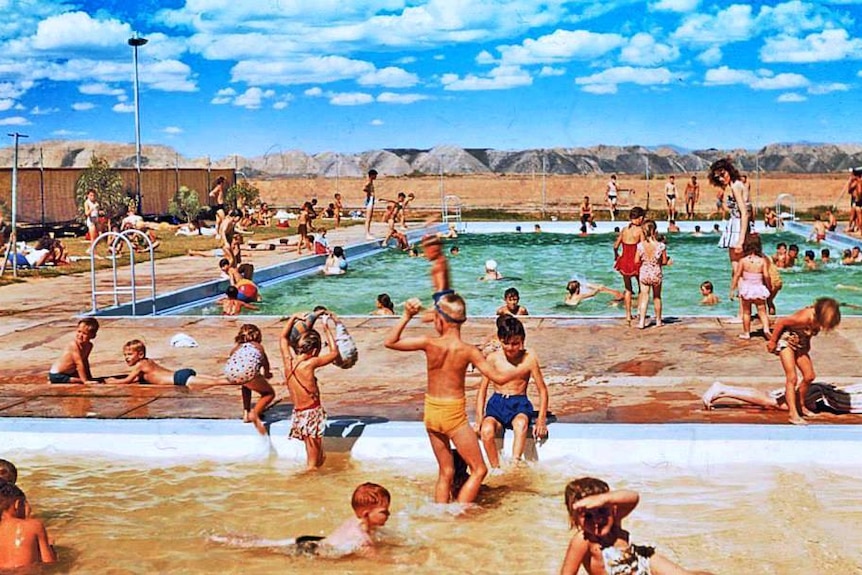 A large swimming pool filled with people with large hills in the background.