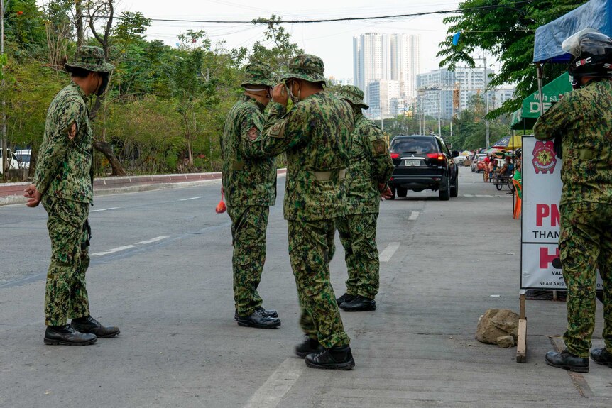 A group of soldiers standing on a street in camouflage gear with face masks on