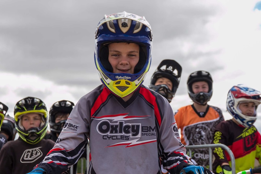 Children in BMX helmets and gear sit on their bikes waiting to ride