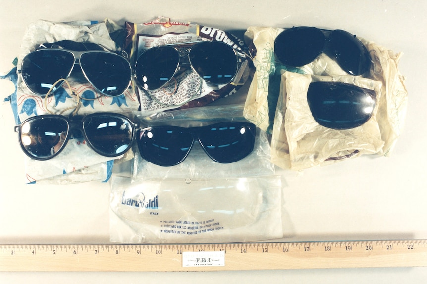 Six pairs of sunglasses lay on a bench next to a ruler