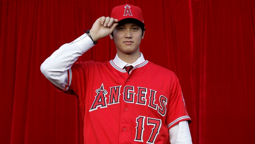 Japanese Los Angeles Angels star Shohei Ohtani tipping his cap in front of a red curtain
