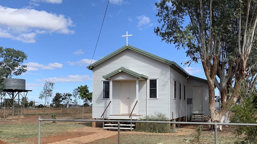 A small, squat white church with green trimming stands under a blue sky