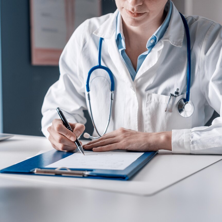 A doctor wearing a white coat and a stethoscope writes on a clipboard.