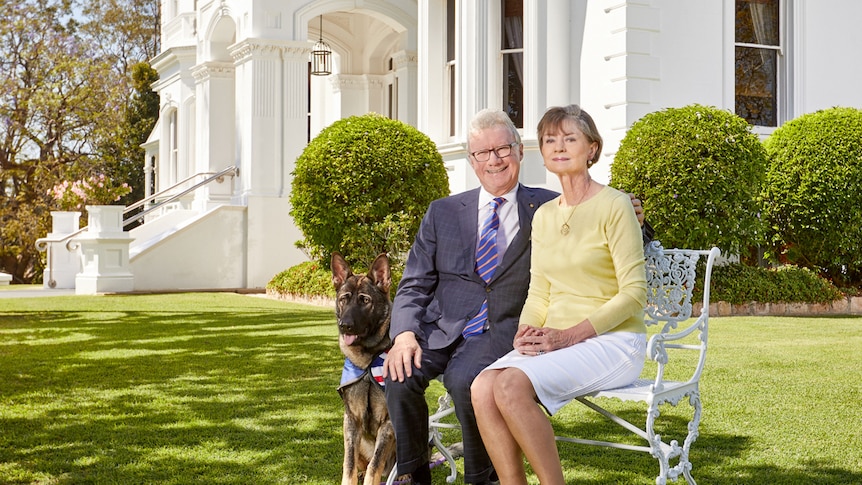 Governor Paul de Jersey and his wife Kaye de Jersey sitting in the front garden of Government House with their dog.