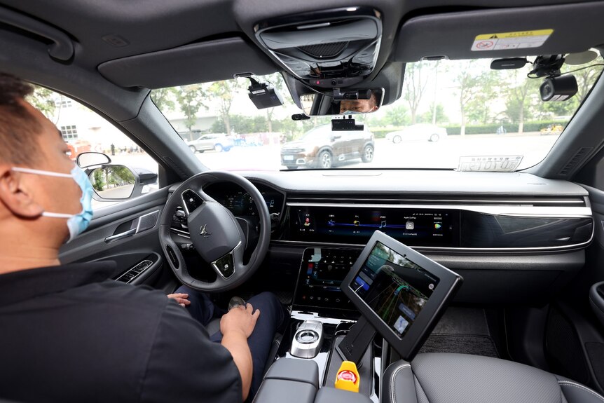 A man sits in the driver's seat of a car that's driving itself