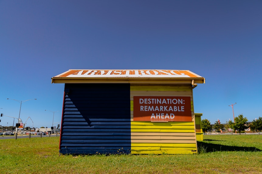 A blue and yellow cottage in a field used as a landmark for Armstrong Creek on a sunny blue sky day. 