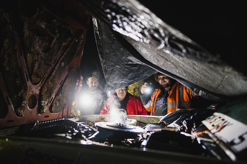 Men working at night with a torch on a cars engine