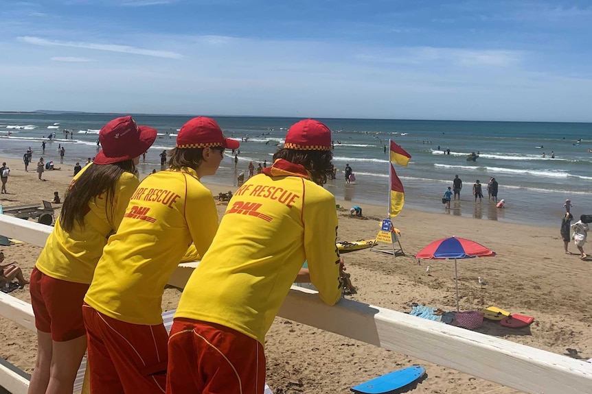 Three lifesavers lined up watching over a busy beach at Ocean Grove.